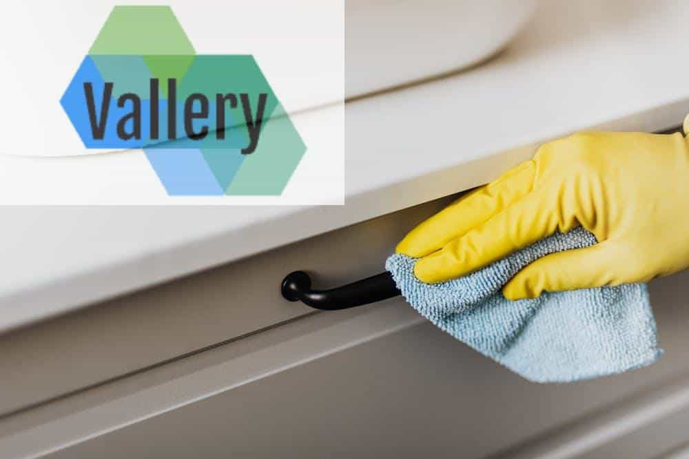 From above of crop faceless person in yellow gloves cleaning handle of cabinet with microfiber cloth in modern bright bathroom