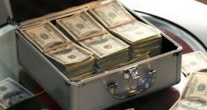 Qué es el crowdlending y cómo funciona esta alternativa financiera Open briefcase filled with stacks of hundred dollar bills on a glass table, representing wealth.