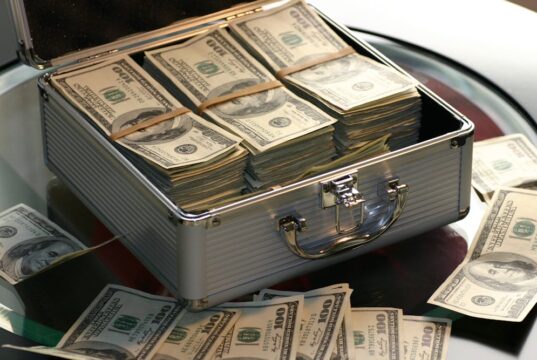 Qué es el crowdlending y cómo funciona esta alternativa financiera Open briefcase filled with stacks of hundred dollar bills on a glass table, representing wealth.